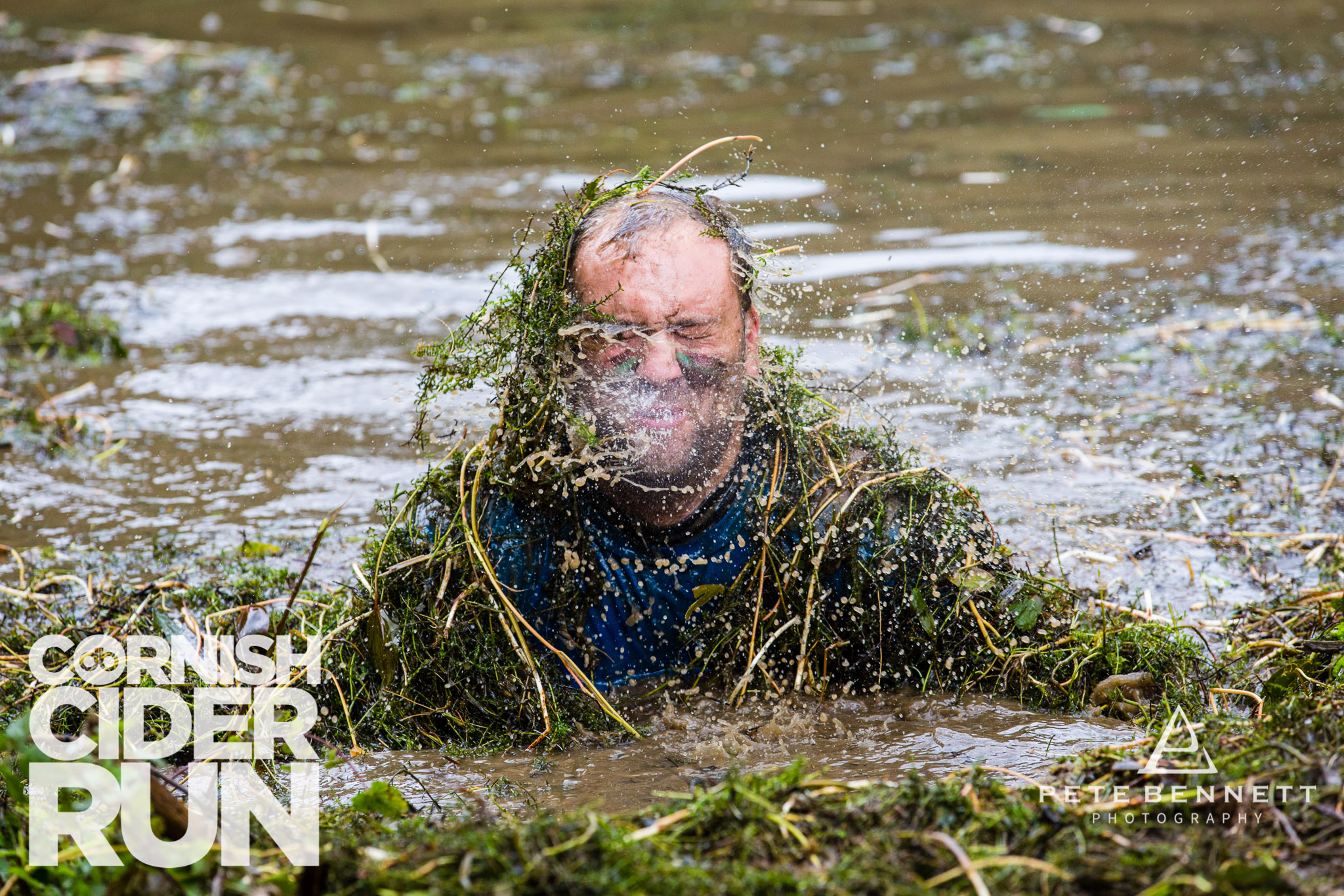 Man covered in weeds getting out of a pond in the cornish cider run 2017