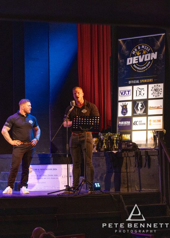Results being announced on stage in front of the official sponsors banner at Devonport Playhouse